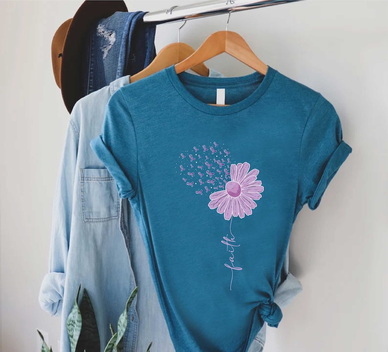May include: Teal blue t-shirt with a purple flower design. The flower is made up of purple ribbon symbols and the word "faith" is written below the flower.