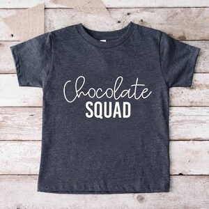 Peut inclure: Un t-shirt gris fonc&eacute; avec le texte "Chocolate Squad" en lettres blanches.