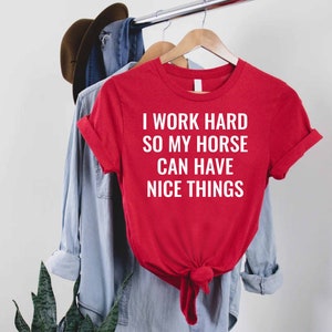 Może przedstawiać: Czerwony T-shirt z białym napisem: "Pracuję ciężko, żeby m&oacute;j koń miał fajne rzeczy."