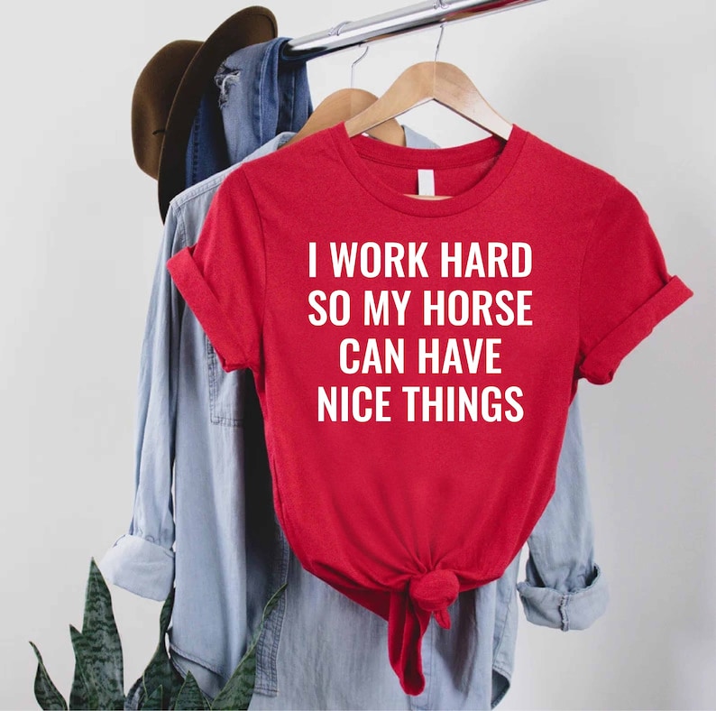 Może przedstawiać: Czerwony T-shirt z białym napisem: "Pracuję ciężko, żeby m&oacute;j koń miał fajne rzeczy."