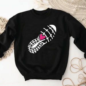 Peut inclure: Sweat-shirt noir avec un graphique blanc d'une chaussure de course avec un c&oelig;ur rose au milieu.