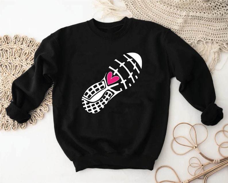 Peut inclure: Sweat-shirt noir avec un graphique blanc d'une chaussure de course avec un c&oelig;ur rose au milieu.