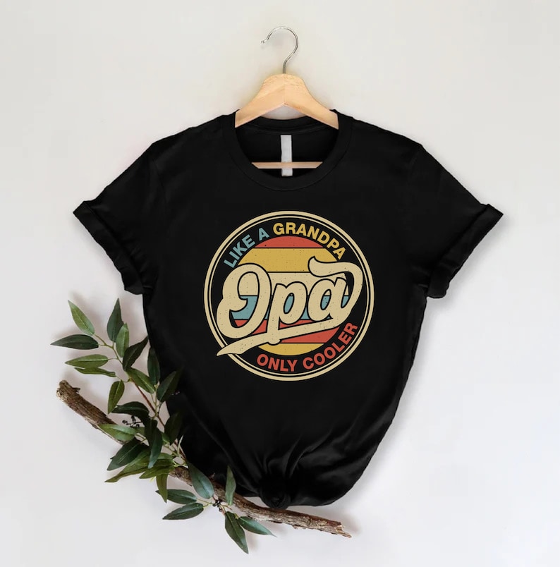 May include: Black t-shirt featuring a vintage-style graphic that reads "Like a Grandpa, Only Cooler" with the word "Opa" in a large, stylised font.