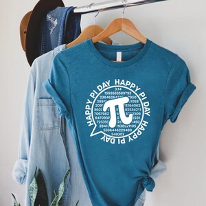 Puede incluir: Una camiseta azul turquesa con un gr&aacute;fico blanco de un globo de di&aacute;logo que contiene el texto "Happy Pi Day" y un gran s&iacute;mbolo pi blanco rodeado de los d&iacute;gitos de pi.
