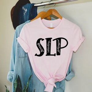 Puede incluir: Camiseta rosa con las letras "SLP" en negro, con las palabras "speech", "language" y "pathologist" escritas verticalmente dentro de las letras.
