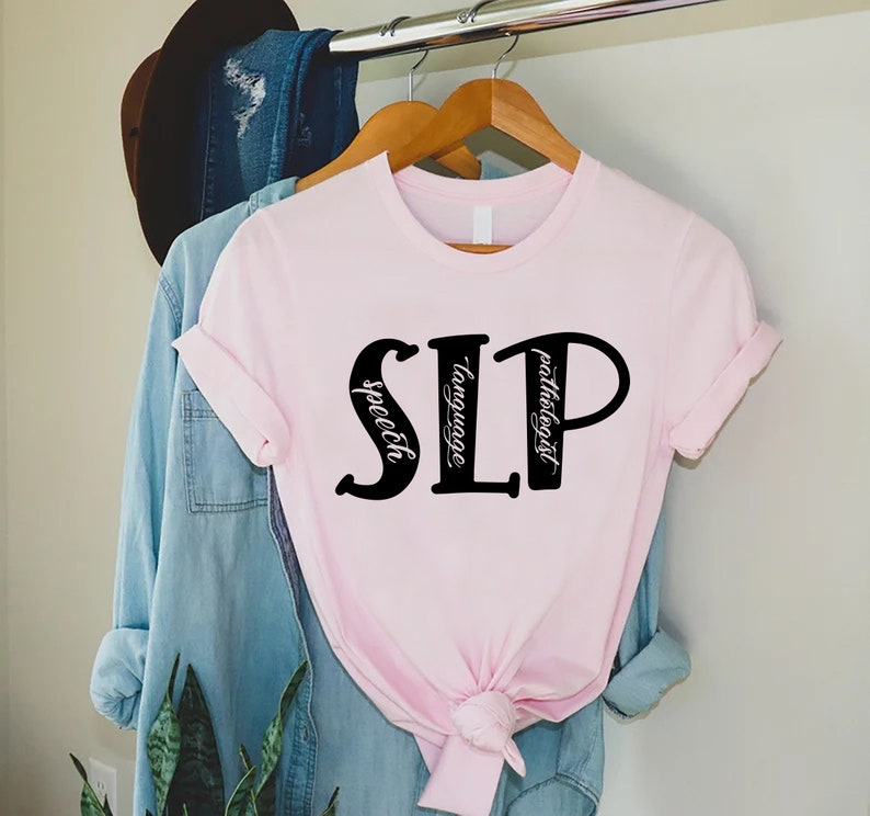 Puede incluir: Camiseta rosa con las letras "SLP" en negro, con las palabras "speech", "language" y "pathologist" escritas verticalmente dentro de las letras.