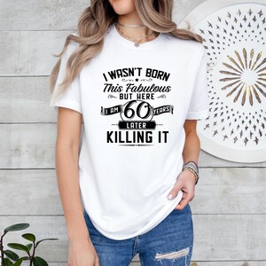 May include: White t-shirt with black text that reads "I wasn't born this fabulous but here I am 60 years later killing it".