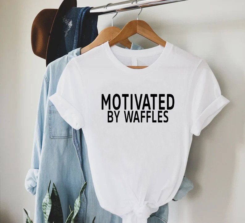 K&ouml;nnte beinhalten: Wei&szlig;es T-Shirt mit schwarzem Text, der "Motiviert durch Waffeln" lautet.