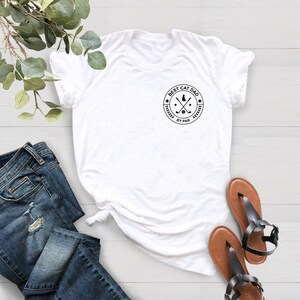 May include: White t-shirt with a circular graphic that reads "BEST CAT DAD BY PAR" in black. The graphic includes a cat silhouette, crossed golf clubs, and stars. The shirt is paired with blue jeans and brown sandals.