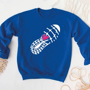 Peut inclure: Un sweat-shirt bleu royal avec un contour blanc de la semelle d'une chaussure de course &agrave; pied avec un c&oelig;ur rose au centre.