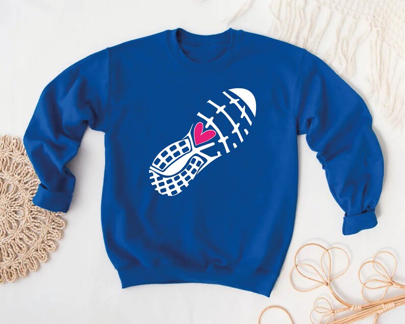 Peut inclure: Un sweat-shirt bleu royal avec un contour blanc de la semelle d'une chaussure de course &agrave; pied avec un c&oelig;ur rose au centre.