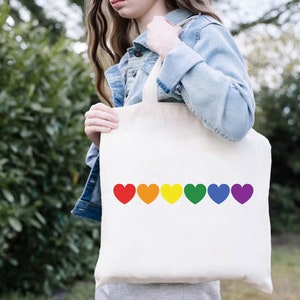 May include: A white tote bag with a rainbow of hearts printed on the front. The hearts are red, orange, yellow, green, blue, and purple.