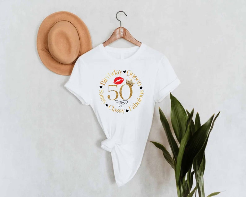 May include: White t-shirt with a gold glitter design that says "Birthday Queen 50 Sassy Classy Fabulous" with a red lip and a gold crown.