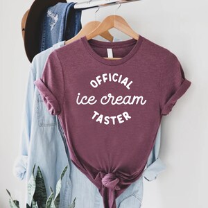 Puede incluir: Una camiseta color granate con el texto "OFFICIAL ice cream TASTER" en blanco.