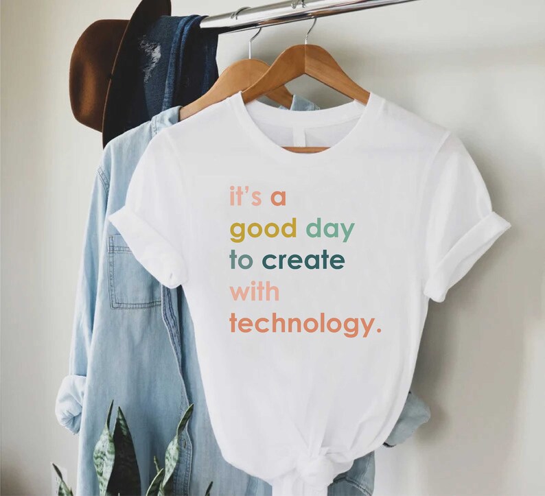 May include: White t-shirt with the text "it's a good day to create with technology." in colourful letters.