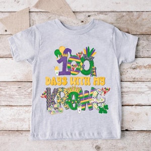 May include: A grey t-shirt with a colourful design featuring the text "100 Days With My Krewe". The design includes Mardi Gras themed elements like beads, a jester hat, and a king cake.