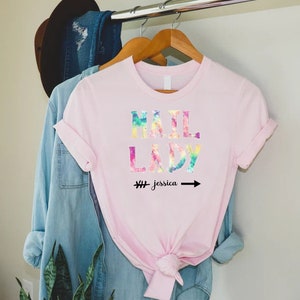 May include: Pink t-shirt with a tie-dye design that says "Mail Lady" with an arrow pointing to the right and the text "# Jessica" underneath.