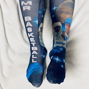 Op de afbeelding: Kniehoge sokken met een denim-achtige achtergrond. De linkersok heeft de tekst "MR BASKETBALL" in het wit. Beide sokken tonen afbeeldingen en tekst, met blauwe en witte sterrenpatronen. Een opvallend mode-item.