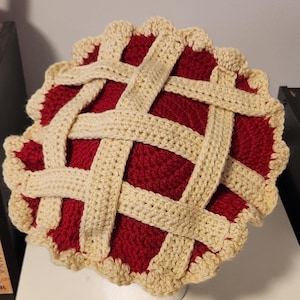 Peut inclure: Un chapeau en crochet en forme de tarte avec une garniture rouge et une croûte beige. Le chapeau est en forme de tarte et a un design de croûte tissée.