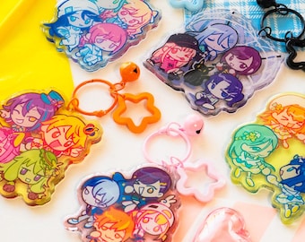 May include: A collection of colorful acrylic keychains featuring anime-style characters. Each keychain has a unique design with multiple characters, attached to a ring with a charm. The keychains are in various shapes, including stars and hearts.
