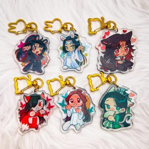 Puede incluir: Seis llaveros de personajes de anime coloridos con anillos de metal dorado. Cada llavero presenta un personaje diferente con diseños y colores únicos. Los personajes están representados en un estilo de dibujos animados con ojos grandes y rasgos expresivos.