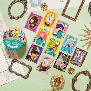 May include: A collection of decorative stamps and washi tape featuring anime-style illustrations. The stamps are in various colors and designs, with characters in teal and black outfits. The washi tape roll has the text "Atelier Studies" and "JOYLYCHI".