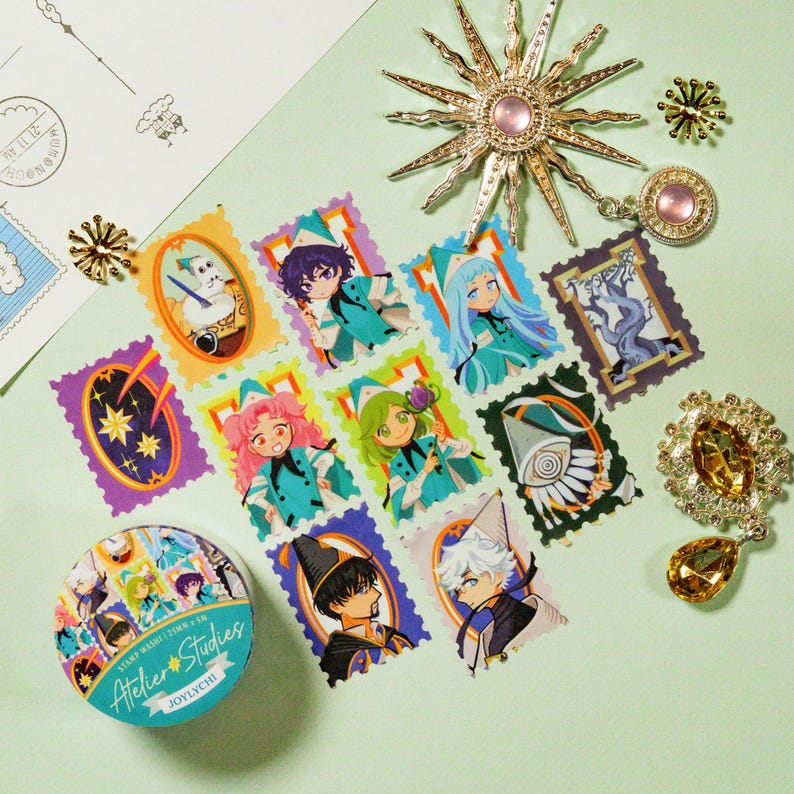 Puede incluir: Una colecci&oacute;n de elementos decorativos que incluye sellos, un rollo de cinta washi y varios broches. Los sellos presentan ilustraciones coloridas de estilo anime. El rollo de cinta washi est&aacute; etiquetado como "Atelier Studies". Los broches son dorados con detalles en rosa y amarillo.