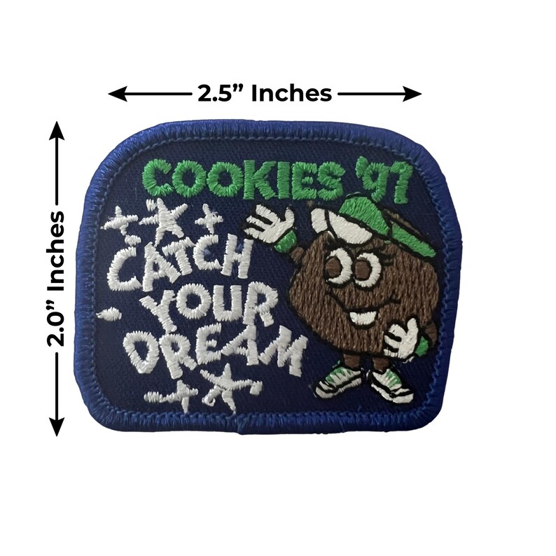 K&ouml;nnte beinhalten: Ein marineblauer, gestickter Aufn&auml;her, 6,35 cm breit und 5,08 cm hoch, mit dem Text "COOKIES '97" und "CATCH YOUR DREAM" in Wei&szlig; und Gr&uuml;n. Er zeigt eine Cartoon-Keksfigur mit gr&uuml;nem Hut und Turnschuhen.