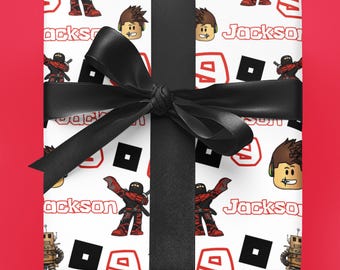 May include: Gift-wrapped present with white wrapping paper featuring a repeating pattern of cartoon characters, the name "Jackson" in red, and black squares. A black ribbon and bow secure the gift, set against a red background.