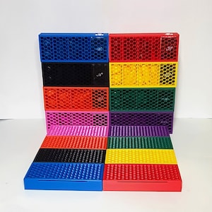 May include: A set of 12 colorful storage boxes with a honeycomb pattern. The boxes are stacked in a pyramid shape and are made of plastic. The boxes are in the following colors: blue, black, orange, pink, purple, green, yellow, and red.