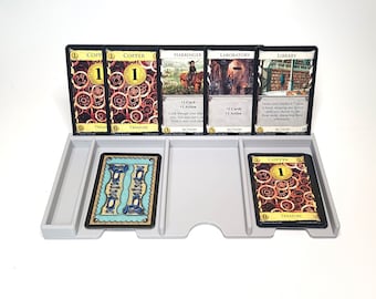 Puede incluir: Primer plano de una configuración de juego de cartas de Dominion con una variedad de cartas que incluyen Copper, Harbinger, Laboratory y Library. Las cartas están dispuestas en una bandeja con una sola carta de Copper en el centro.