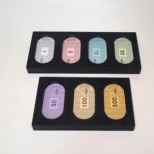 May include: Two black plastic trays with slots for holding game pieces. The top tray has four slots with the numbers 1, 5, 10, and 20. The bottom tray has three slots with the numbers 50, 100, and 500.