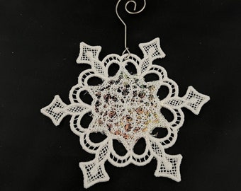 May include: White lace snowflake ornament with a silver wire hanger. The snowflake is intricate and delicate, with a slightly iridescent sheen.