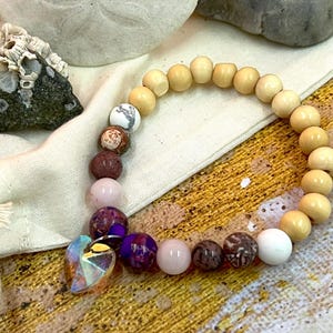 May include: A bracelet with wooden beads and various gemstone beads, including pink, purple, and brown. A crystal heart charm hangs from the bracelet.
