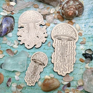 May include: Three wooden laser cut jellyfish ornaments with intricate designs. The jellyfish are in various shades of brown and have a natural wood finish.