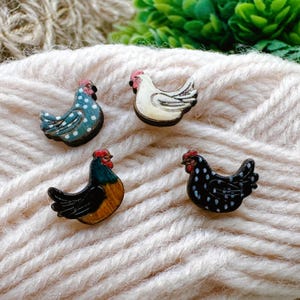 May include: Four wooden chicken-shaped embellishments. One is white with black accents, another is blue with white polka dots, and the other two are black with white polka dots and a rooster with a red comb. These are likely for crafting or scrapbooking.