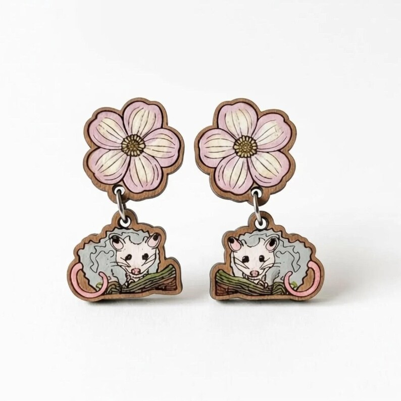 A pair of earrings featuring a cute cartoon cat and a pink flower design.