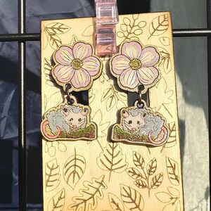 a pair of earrings with a floral design, hanging on a metal frame.