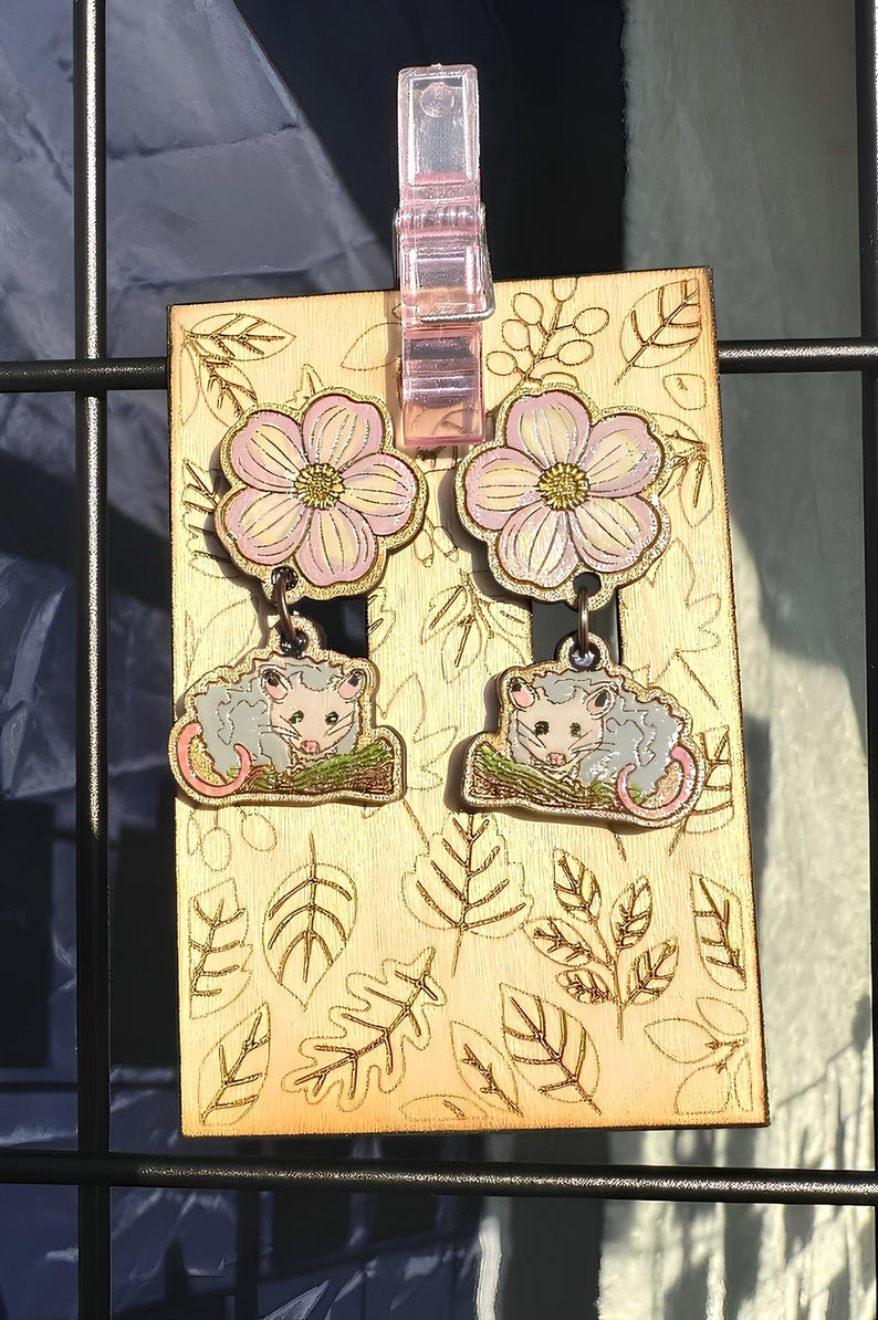 a pair of earrings with a floral design, hanging on a metal frame.