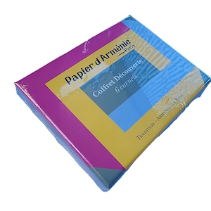 May include: A square box with a colourful design, wrapped in clear plastic. The box features a yellow, blue, and pink colour scheme. Text on the box reads "Papier d'Arménie Paris" and "Coffret Découverte 6 carnets."