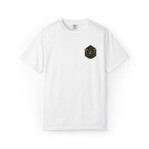 May include: White t-shirt with a small, colourful patch on the chest. The patch features a geometric design with green, orange, and black elements. The shirt has a crew neck and short sleeves, suitable for casual wear.