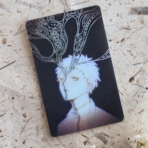 May include: A rectangular card featuring a black background with a stylized illustration of a person with short white hair. Silver line art extends from the person's forehead upward. The text Marshmallow is printed in small white letters on the left.