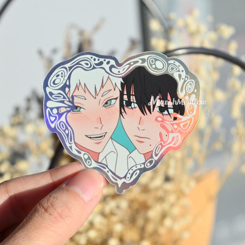 May include: Holographic heart-shaped sticker featuring two anime-style characters. One character has white hair and the other has black hair. The sticker has a decorative border and the text "MarshMeadow".