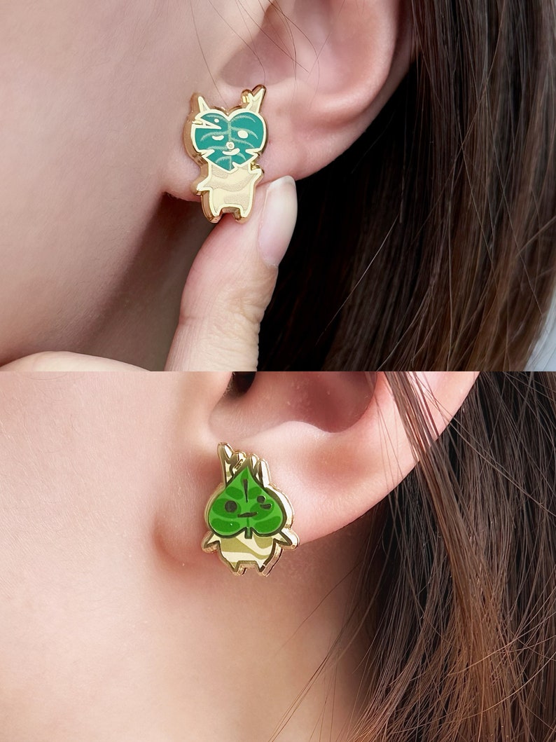 May include: Gold-tone earrings featuring a cartoon character with a green leaf on its head. The character is wearing a white and brown striped shirt.