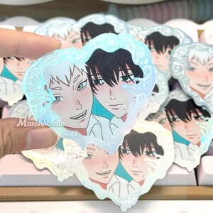 May include: Holographic heart-shaped stickers featuring anime-style illustrations of two male characters. One character has white hair and the other has black hair. The stickers have a water-like border and the text "MarshMeollow".