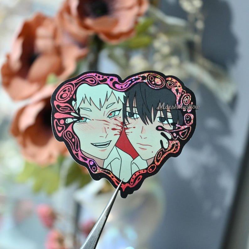 May include: A heart-shaped sticker featuring two anime-style characters with light and dark hair. The sticker has a pink and glittery border with the text "MarshMeollow". The characters have red accents on their faces.
