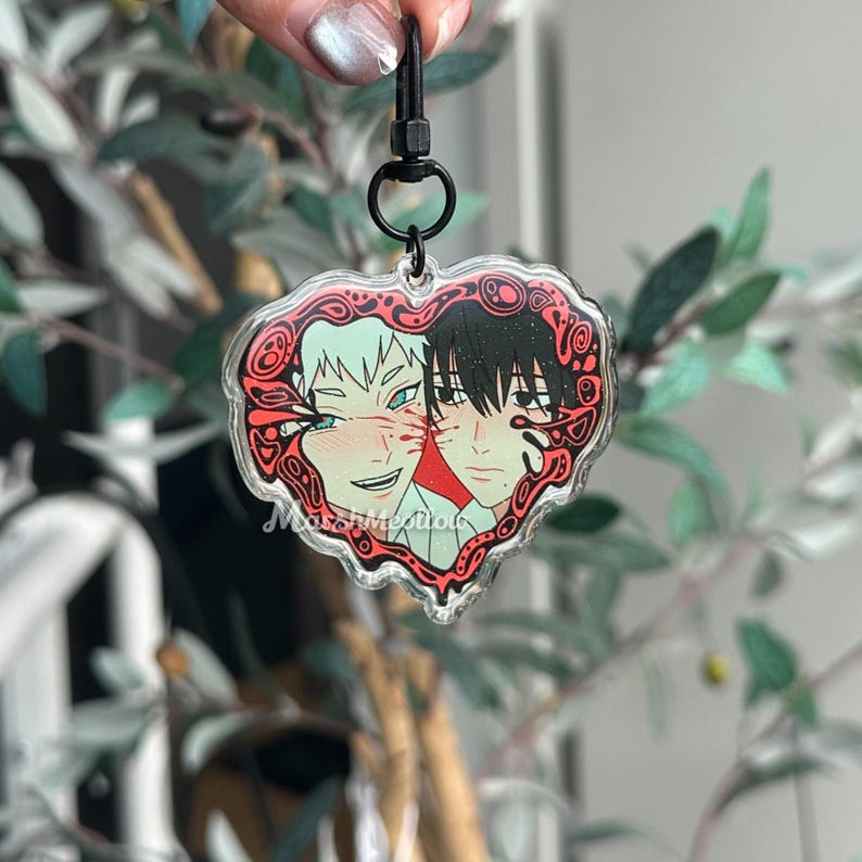K&ouml;nnte beinhalten: Ein herzf&ouml;rmiger Acryl-Schl&uuml;sselanh&auml;nger mit zwei Anime-Charakteren. Ein Charakter hat wei&szlig;es Haar und der andere hat schwarzes Haar. Der Schl&uuml;sselanh&auml;nger hat einen roten Zierrand und einen schwarzen Verschluss.