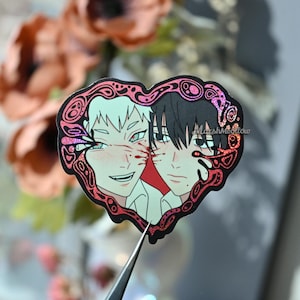 May include: A heart-shaped sticker featuring two anime-style characters. One character has white hair and the other has black hair. Both characters have blood-like markings. The sticker has a pink and red border with the text "MarshMellow".