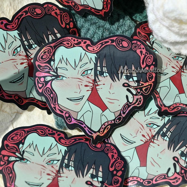 May include: Heart-shaped stickers featuring anime-style illustrations of two male figures. One has black hair, the other white. Both have red accents and are framed by a red glitter design. The text "MarshMeollow" is visible.