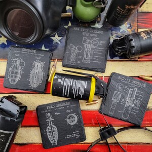 May include: A collection of black slate plaques with white text and illustrations of different types of grenades. The plaques are labeled "M84 STUN GRENADE", "FRAG GRENADE", "RGD-33 GRENADE", and "GRENADE".